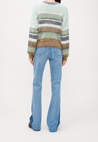Strickpullover mit bunten horizontalen Streifen in Grün, Braun und Grau. Kombiniert mit hellblauen Flared Jeans mit seitlichen Schlitzen.