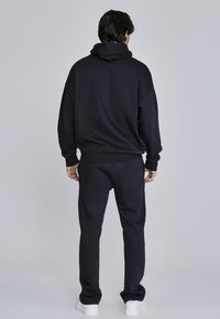 Črna kapuca in trenirka iz mehkega materiala, ohlapnega kroja, z mrežastimi manšeti in pasom, z kenguru žepom in brez vidnih logotipov.