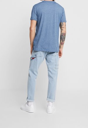 T-shirt à manches courtes bleu chiné, coupe décontractée, associé à un pantalon cargo bleu clair avec des poches latérales et des accents en rouge et blanc. Baskets blanches.
