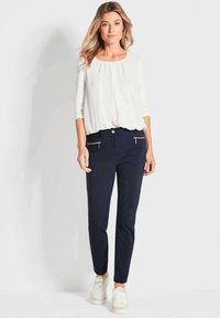 Witte top met een ronde halslijn en driekwart mouwen, gecombineerd met navy slim-fit broek met ritszakken en witte sneakers.