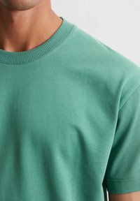 Korte mouw, ronde hals t-shirt van effen groene katoen. Voorzien van een gladde textuur met een ribgebreide halslijn, en subtiele stiksels.