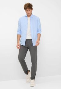 Lichtblauwe linnen overhemden met knopen over een wit T-shirt, gecombineerd met grijsgelockte slim-fit broek en witte sneakers. Eenvoudige, casual outfit.