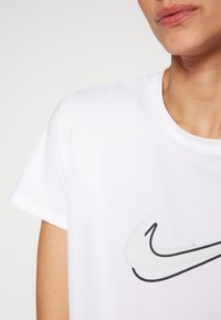 Hvit t-skjorte med korte ermer som har et Nike-logo i svart og grått. Glatt tekstur med rund hals, tilpasset passform og ingen mønstre.