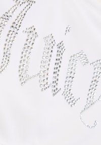 Witte stof met zilveren strass embellishments die een gestileerd tekstpatroon vormen, met stenen van verschillende maten voor textuur en glans.