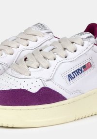 Sneakers in pelle bianca con accenti in suede viola, punta tonda, dettagli perforati e suola in gomma beige. Presentano lacci intrecciati e una patch con logo.