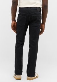 Black denim jeans with a straight-leg fit, featuring two back pockets, a branded waistband, and stitched detailing.