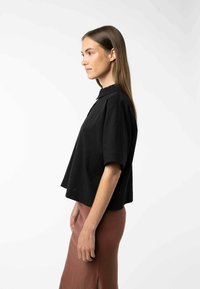 Zwarte kortearmige collshirt met een relaxte pasvorm en een gestructureerde stof, gecombineerd met een aansluitende bruine rok met een zijsplit.