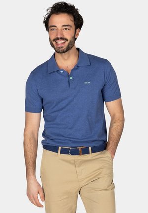 Blauwe polo met korte mouwen en een gestructureerde afwerking, met een kraag, een groene accentknop en een klein logo op de borst. Beige broek en riem.
