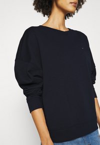 Sudadera azul marino en un material suave y texturizado. Cuenta con hombros caídos, puños acanalados y un pequeño logo en el pecho.