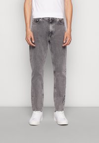 Jeans de mezclilla gris con un corte relajado, que presentan un diseño de cinco bolsillos, un desgaste sutil y piernas rectas, combinados con zapatillas blancas.