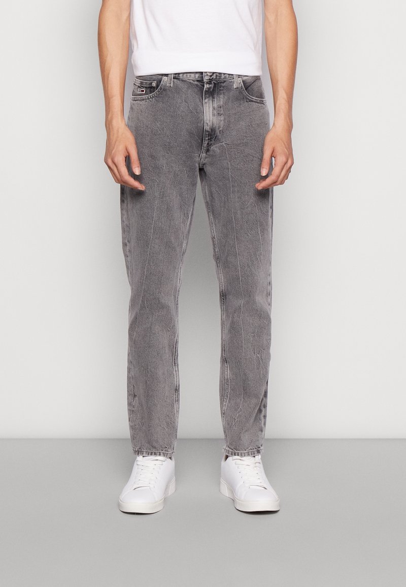 Jeans de mezclilla gris con un corte relajado, que presentan un diseño de cinco bolsillos, un desgaste sutil y piernas rectas, combinados con zapatillas blancas.