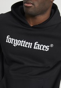 Black hooded sweatshirt made of soft fabric, featuring bold white text "forgotten faces" and logo on the front, with a kangaroo pocket.