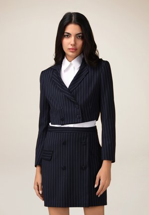 Blazer a rayas marinas con un diseño corto y botones de doble botonadura, combinado con una falda a juego que cuenta con dos bolsillos frontales.