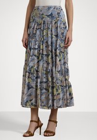 Fustă maxi florală cu volane în straturi, având nuanțe de albastru, verde și bej. Fabricată dintr-un material ușor. Asortată cu sandale cu toc maro.
