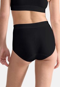 Zwarte high-waisted onderbroek gemaakt van een soepel elastisch materiaal, met een brede tailleband en een naadloos ontwerp voor comfort.