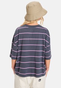 T-shirt gris surdimensionné avec des rayures horizontales roses, col rond et manches courtes. Présente une patch logo au dos.