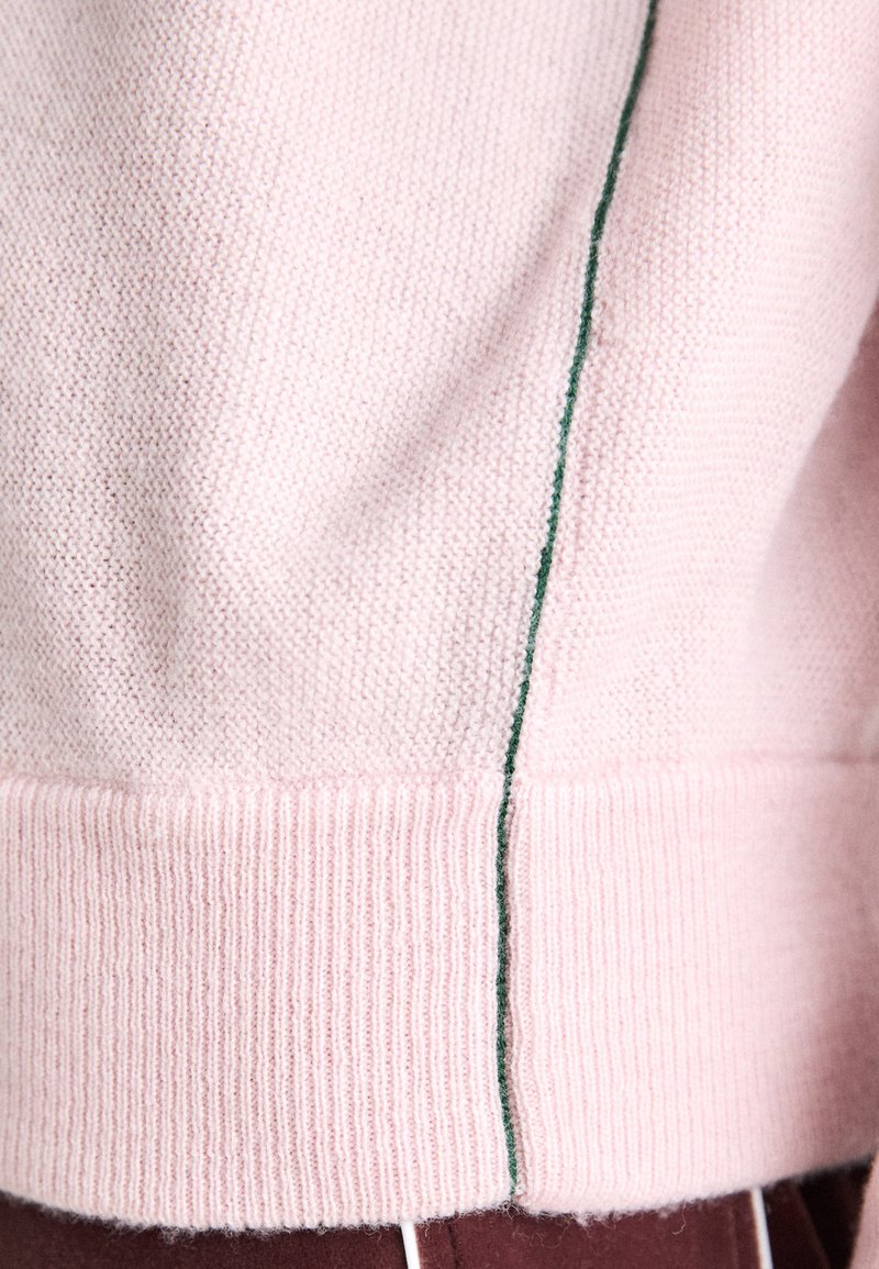 Rosa gestrickter Pullover mit strukturiertem Oberflächen, ausgestattet mit einer kontrastierenden grünen vertikalen Naht und gerippten Bündchen. Weicher Stoff, lässiges Design.