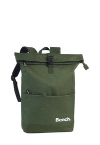 Sac à dos vert à rabat fabriqué en tissu durable avec des bretelles ajustables. Comprend une poche avant et un imprimé de logo blanc en bas.