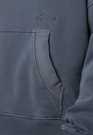 Dunkelgraue Sweatshirt-Tasche mit geripptem Saum und dezent besticktem Markennamen über der Tasche auf weichem Baumwollstoff.