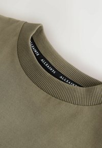 Detailný záber na olivovo zelenú mikinu s okrúhlym výstrihom a rebrovaným golierom, s čiernou vnútornou štítkom s nápisom "ALLSAINTS" v bielom texte.