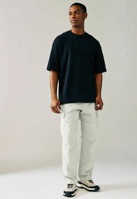 Camiseta negra de gran tamaño, pantalones cargo gris claro con bolsillos laterales y zapatillas negras/crema. Tejido suave, corte relajado y diseño casual.