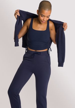 Marineblaues Sportoutfit mit einem gerippten Crop-Top und passenden Jogginghosen mit verstellbarem Bund und enganliegendem Saum. Glatte Textur.