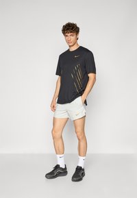 Nike athletic outfit featuring a dark gray shirt with gold accents and light gray shorts. Set against a plain background, footwear is black.