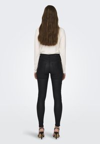 Zwarte skinny jeans met een hoge taille, gladde textuur en achterzakken. Gepaard met een langemouwen top en hoge hakken sandaaltjes.