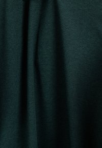 Donkergroene stof met een gestructureerd ribbelpatroon, met subtiele plooien die diepte creëren. Het materiaal lijkt lichtgewicht en glad.