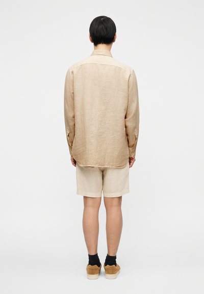 Ελαφρύ πουκάμισο λίνου σε ανοιχτό μπεζ χρώμα με μακριά μανίκια, συνδυασμένο με ανάλαφρα σορτς στο ίδιο χρώμα. Casual εφαρμογή και μινιμαλιστικός σχεδιασμός. Το σύνολο ολοκληρώνουν παπούτσια από σουέντ.