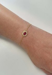 Bracciale in oro con al centro un gemma rossa ottagonale circondata da piccole pietre chiare, posato su un polso.