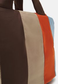 Sac fourre-tout rectangulaire en panneaux marron, beige, orange et bleu clair. Fabriqué en tissu lisse et brillant avec des poignées robustes.