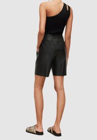 Černé kožené kraťasy s hladkou strukturou, středním pasem a bočními kapsami. Doplněné černým tílkem bez rukávů s jedinečným designem na zádech.