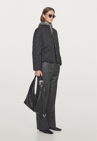 Black quilted jacket with gray fleece lining, worn with gray high-waisted trousers. Holding a black leather handbag with a silver accent.