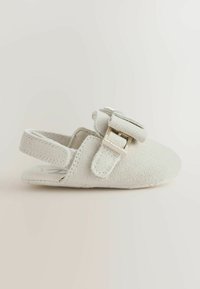 Samtiges Babyschuh in Cremefarbe mit verstellbarer Schnalle und offenem Fersenriemen auf hellem Hintergrund.