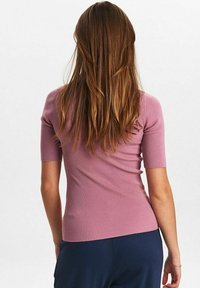 Ribbad rosa kortärmad topp med en figurnära silhuett, slät textur och rund halsringning, i kombination med marinblå byxor. Bakifrån betonas.