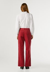 Sarkana korduroja platā kāja, vertikāla tekstūra, augsta josta un divas aizmugurējās kabatas. Apvienota ar baltu krekla blūzi ar apkakli.