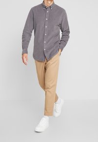 Camisa de botones de pana gris con botones blancos, combinada con pantalones tapered beige y zapatillas blancas. Diseño sencillo con un corte clásico.