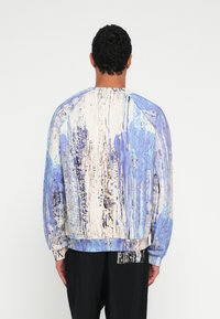 Sininen ja kermaan vivahtava neule, jossa on abstrakti valumakuviiointi, raglanhihat sekä resorikanttaukset hihansuissa ja helmassa. Valmistettu pehmeästä kankaasta.