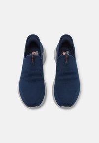 Marine slip-on sneakers med teksturert strikket overdel, grå gummisåle og oransje Skechers-logo. Lett og pustende design.