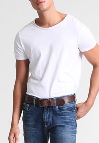 Witte katoenen t-shirt, ronde halslijn, gecombineerd met blauwe jeans en een bruine leren riem met een metalen gesp voor het vastmaken.