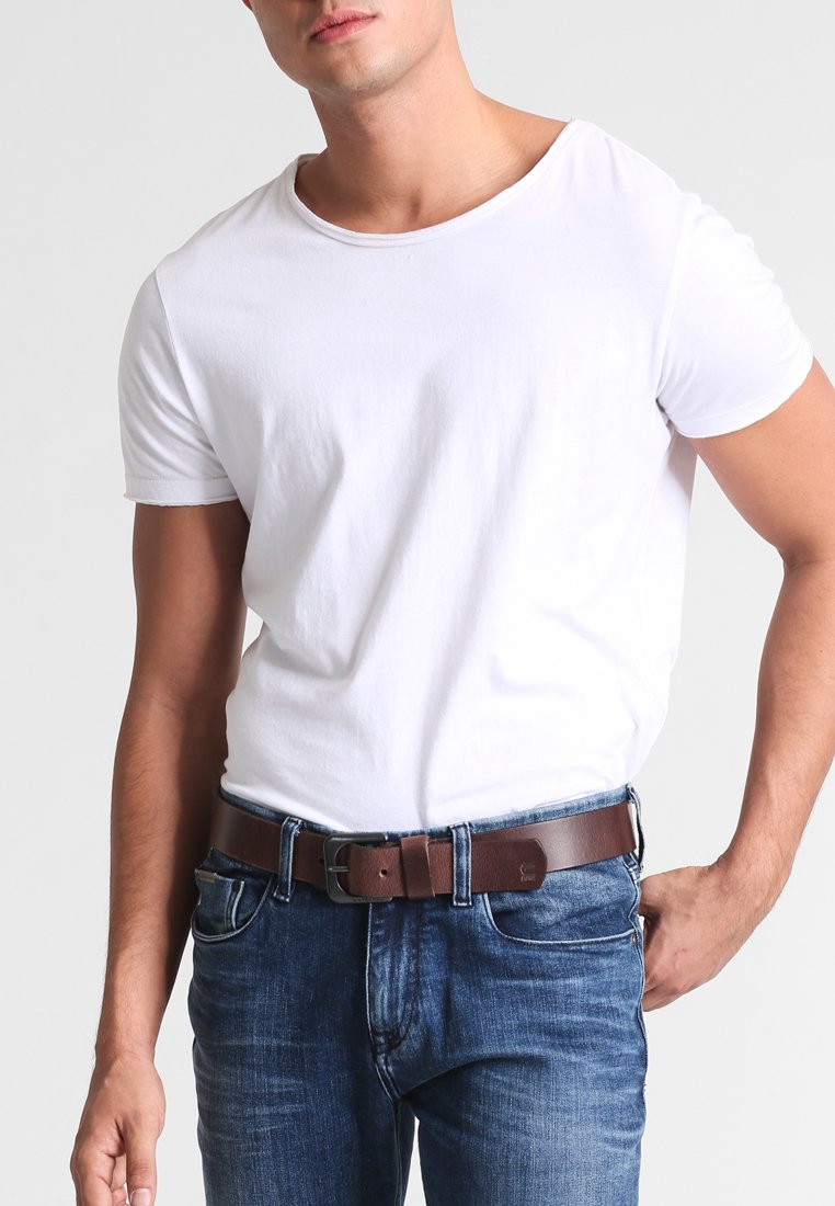 Witte katoenen t-shirt, ronde halslijn, gecombineerd met blauwe jeans en een bruine leren riem met een metalen gesp voor het vastmaken.