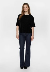 Svart kortärmad velurtopp med rund halsringning, kombinerad med mörka utsvängda jeans och svarta klackskor. Enkelt, rent design.