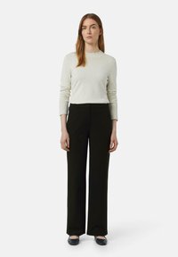 Lichtgrijze trui met geribde manchetten, gecombineerd met een high-waisted zwarte wijde broek en zwarte ballerina's. Eenvoudig ontwerp en neutrale kleuren.