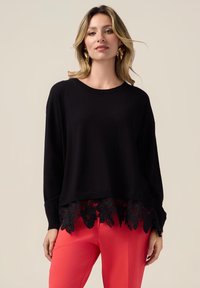 Maglione nero a maglia con scollo rotondo e maniche lunghe, caratterizzato da un orlo con rifinitura in pizzo ondulato e intricati motivi floreali in tonalità scure.