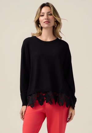 Pull en tricot noir avec un col rond et des manches longues, doté d'une bordure en dentelle festonnée en bas et de motifs floraux complexes dans des tons sombres.