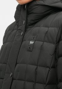 Schwarze gepolsterte Jacke mit hohem Kragen, Knopfverschluss, Stepptextur und einem Markenetikett auf der Vorderseite.