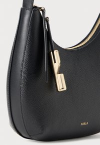 Bolsa de mão preta em couro com textura granulada, apresentando um detalhe em metal dourado e fecho em zip. Logotipo da marca em relevo na lateral.