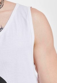 Top de bumbac alb cu decolteu în V și design fără mâneci, având un model grafic negru pe față și cusături curate.