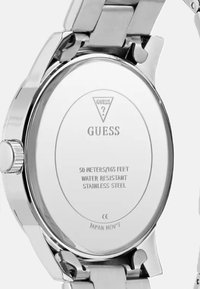 Tylny mechanizm zegarka ze stali nierdzewnej z wygrawerowanym logo marki, szczegółami odporności i gładką, błyszczącą fakturą; okrągły kształt z metalicznym wykończeniem.